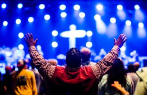 A diverse crowd with arms raised at a vibrant indoor religious concert.